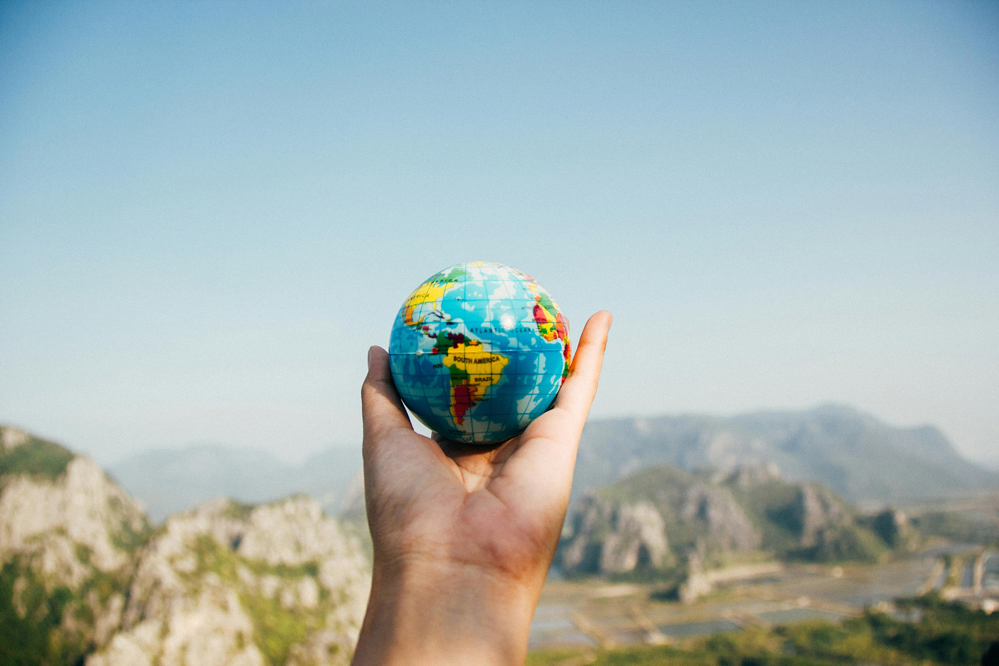 close up shot of hand, outstretched, holding a small globe with out of focus scenic vista in the background