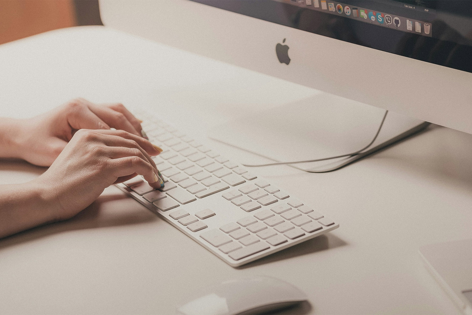 Close up of hands typing on Mac keyboard with iMac on the desk