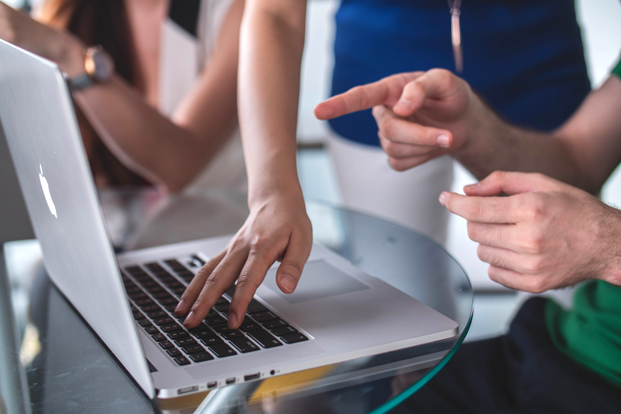 Close up shot of laptop, with a group reviewing details on a laptop, with one hand typing on keyboard. 